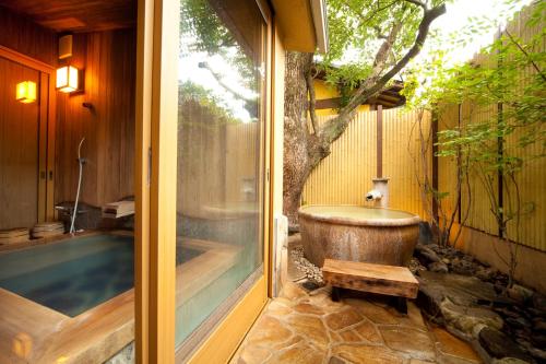 a bathroom with a bath tub next to a tree at Kappo Ryokan Kannawa Bettei in Beppu