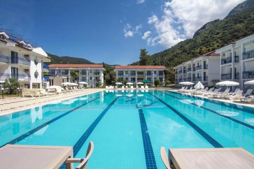 a large swimming pool with chairs and mountains in the background at Belcekum Beach Hotel in Oludeniz