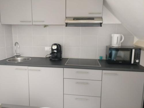 a white kitchen with a microwave and a sink at Greenfee vakantieappartement in De Haan