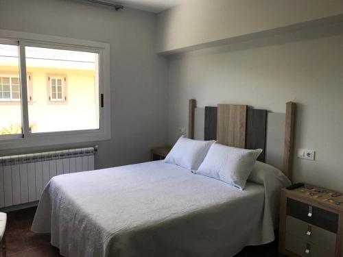 a bedroom with a bed with white sheets and a window at Pensión CHE in O Pedrouzo