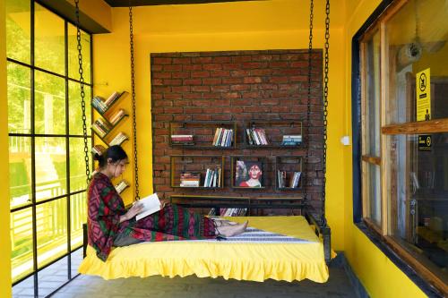 a woman sitting on a bed reading a book at The Hosteller Mcleodganj, Upper Bhagsu in McLeod Ganj