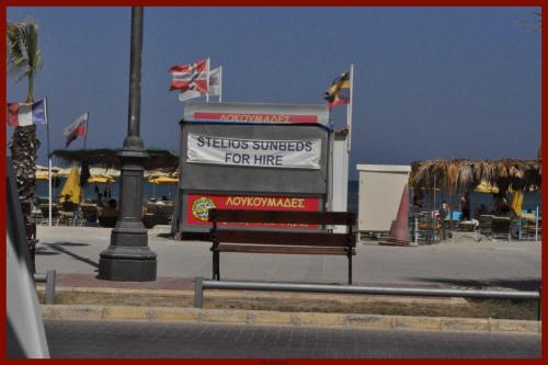 a bench sitting in front of a building with flags at St. George Rent Rooms in Larnaca