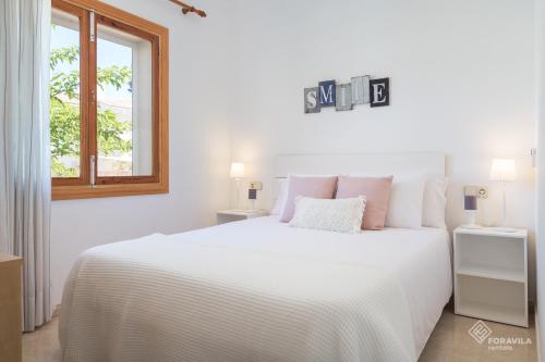 a white bedroom with a large white bed and a window at Berganti in Port d'Alcudia