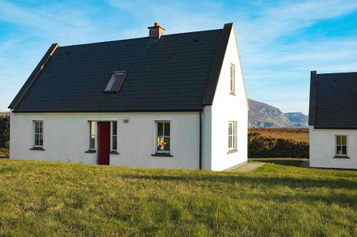 una casa blanca con techo negro en una colina en Butterfly Cottage, en Achill