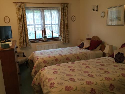 a bedroom with two beds and a tv and a window at Li’le Hullets, 3 Seed Howe Cottages in Staveley