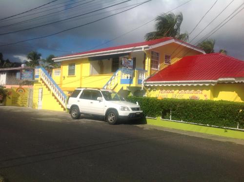 a white car parked in front of a yellow house at Rainbow Beach Apartments & Rooms in Calibishie