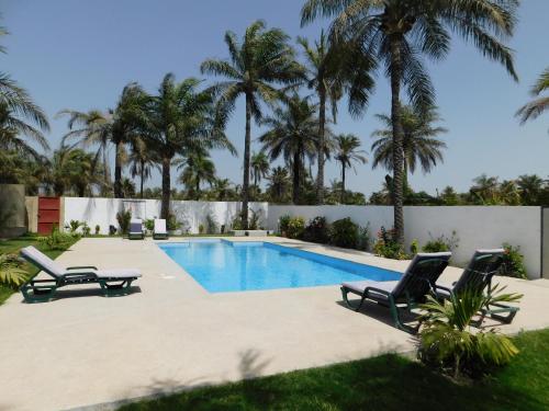 a swimming pool with two lounge chairs and palm trees at CAP BAY in Cap Skirring