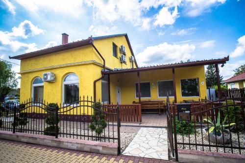 a yellow house with a fence in front of it at Mickey's Thermal Apartments in Tiszakécske