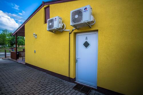 a yellow building with a door and a fan at Mickey's Thermal Apartments in Tiszakécske