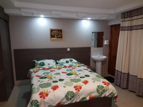 a bedroom with a bed with a floral comforter and a sink at Adala Motel in Meru
