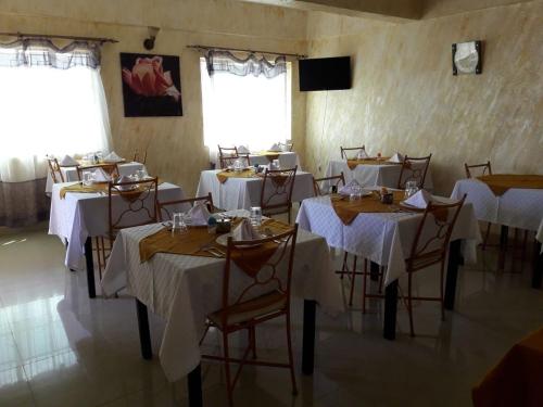 een eetkamer met tafels en stoelen met witte tafellakens bij Adala Motel in Meru