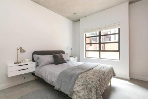 a white bedroom with a bed and a window at Trendy Melrose Apartment in Johannesburg