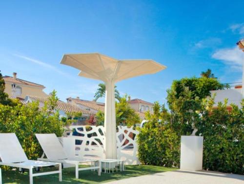 un grupo de sillas blancas y una sombrilla en Hotel Villamor, en Denia