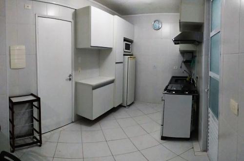 eine kleine Küche mit weißen Schränken und einem Kühlschrank in der Unterkunft Guaruja - Enseada in Guarujá