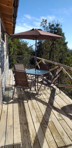 a table and chairs on a deck with an umbrella at Cabañas Latitud 41 Sur in Quillaipe