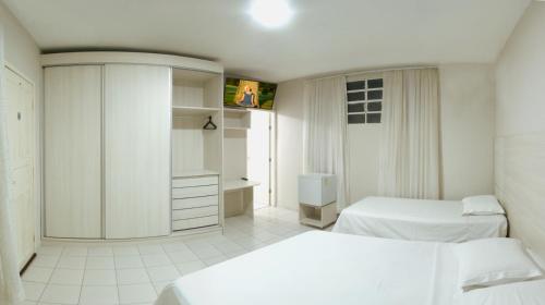 a white bedroom with two beds and a cabinet at Hotel Curitiba Campo Comprido in Curitiba