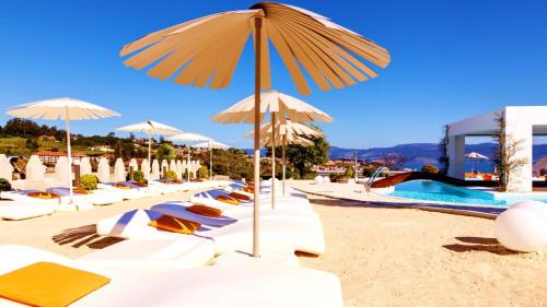 a row of lounge chairs and umbrellas on a beach at Augusta Eco Wellness Resort 4 Superior in Sanxenxo