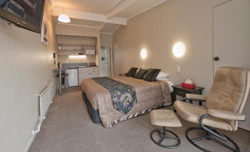 a bedroom with a bed and a chair and a kitchen at Sport Of Kings Motel in Rotorua