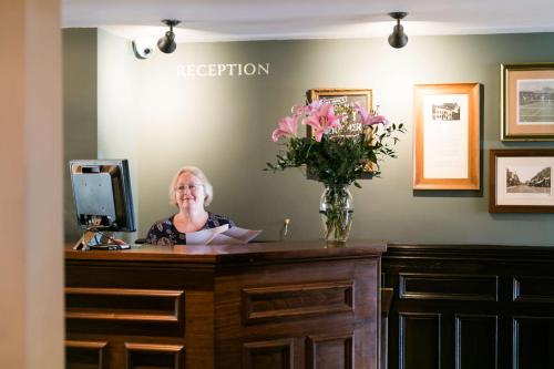 a woman standing in front of a counter with a vase of flowers at Rose And Crown Hotel in London
