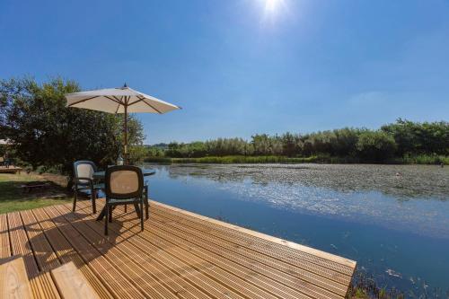 a wooden deck with two chairs and an umbrella at Lynstone Lakes in Bude