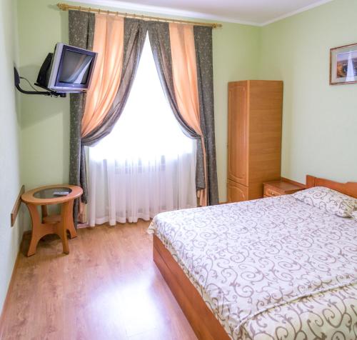 1 dormitorio con 1 cama, TV y ventana en Каприз en Kamianets-Podilskyi