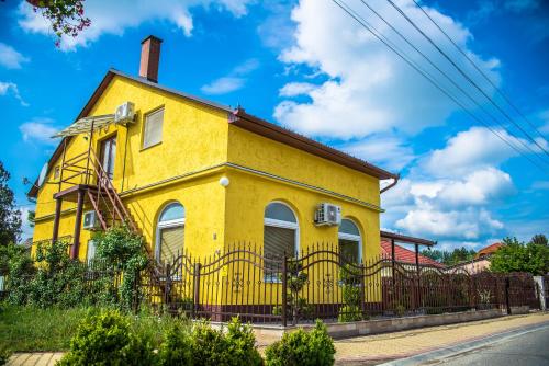 a yellow house with a black fence at Mickey's Thermal Apartments in Tiszakécske