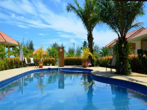 a swimming pool with palm trees and a house at Ao Thai Resort in Sathing Phra