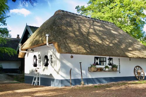 Cabaña con techo de paja y rueda delante de ella en Bakhuisje op de Veluwe en Heerde