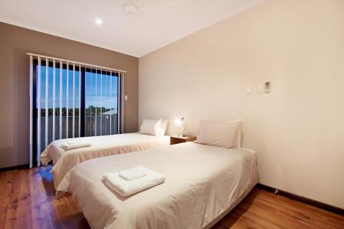 two beds in a room with a large window at Marina Views Townhouse in Darwin
