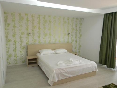 a bedroom with a white bed with green wallpaper at Vila Verda in Eforie Nord