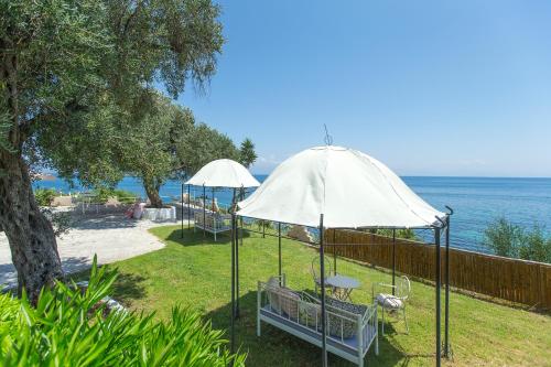 two white umbrellas sitting on the grass near the water at Aurora Beach Hotel in Agios Ioannis Peristeron