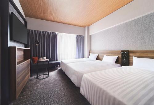a hotel room with two beds and a flat screen tv at RIHGA PLACE HIGOBASHI in Osaka