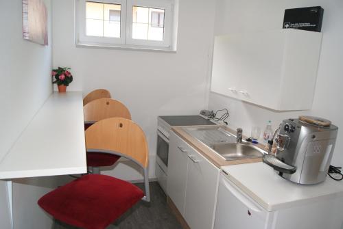 une petite cuisine blanche avec un évier et un fauteuil rouge dans l'établissement Privatzimmer Mitterbacher, à Fohnsdorf