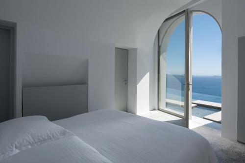 a bedroom with a white bed and a large window at Echoes Luxury Suites in Oia