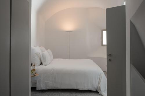 a white bedroom with a white bed and a lamp at Echoes Luxury Suites in Oia