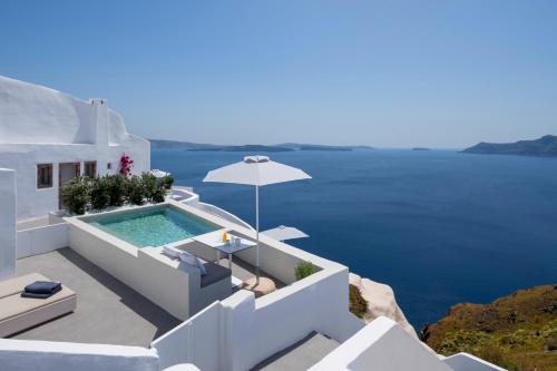 a villa with a swimming pool and an umbrella at Echoes Luxury Suites in Oia