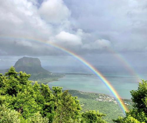 a rainbow over the water with a mountain at Hotel Chalets Chamarel in Chamarel