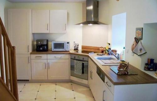 une cuisine avec des armoires blanches et un comptoir dans l'établissement Gîte Le Galta - Maison entiérement équipée, 2 chambres, SdB avec bain à remous, terrasse privative près de la DOLCE VIA, à Saint-Fortunat-sur-Eyrieux