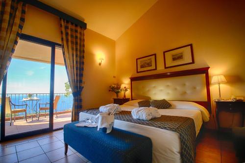 
a hotel room with a large bed and a large window at Capo Dei Greci Taormina Coast Hotel & SPA in Santa Margherita-Sant'Alessio Siculo
