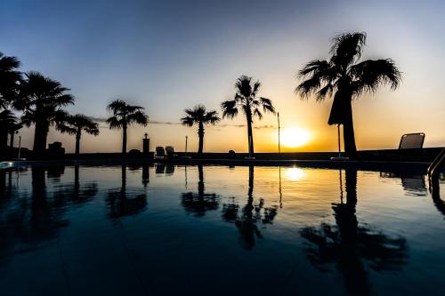 a swimming pool with palm trees and the sunset at Sun Camero Apartments in Pomos