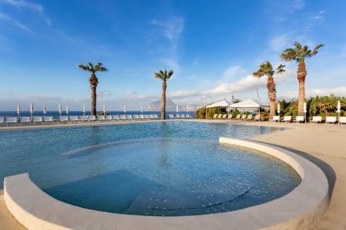 een groot zwembad met palmbomen en de oceaan bij La Tonnara di Bonagia Resort in Valderice