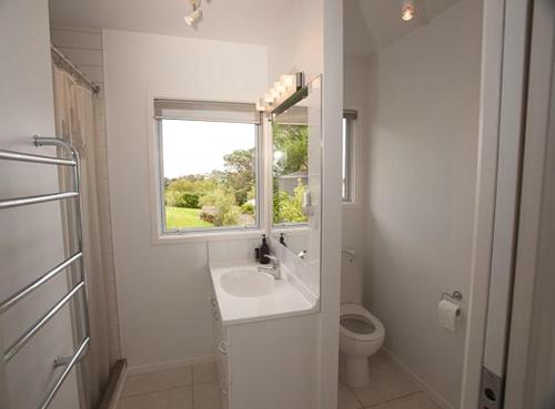 ein weißes Bad mit einem Waschbecken und einem Fenster in der Unterkunft Bayview Retreat in Oneroa