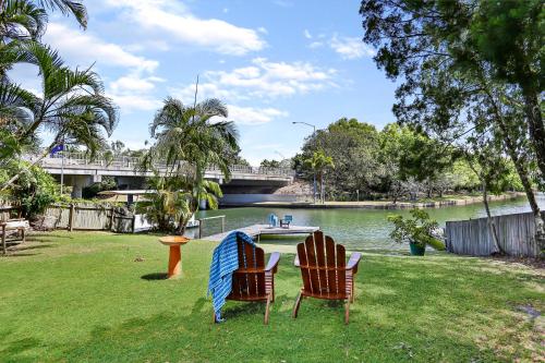 two chairs sitting on the grass next to a river at Clouds End in Noosaville