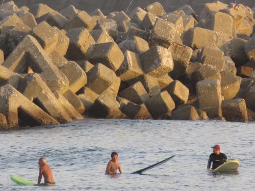 three people sitting on surfboards in the water at 磯ノ浦駅前ゲストハウス 月と空moon and sky in Wakayama