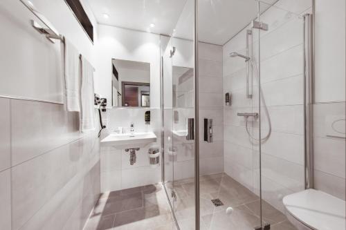 baño blanco con ducha y lavamanos en Maison Schiller by DesignCity Hotels, en Múnich