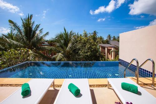 a swimming pool with two white benches in front of a resort at Amatapura Villa 26 in Ao Nam Mao