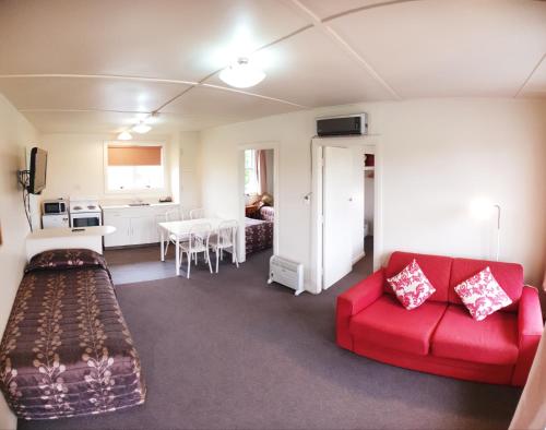 a living room with a red couch and a kitchen at Glacier View Motel - Franz Josef in Franz Josef