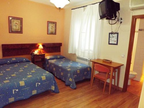 a bedroom with two beds and a desk and a television at Hotel Castilla in Antequera