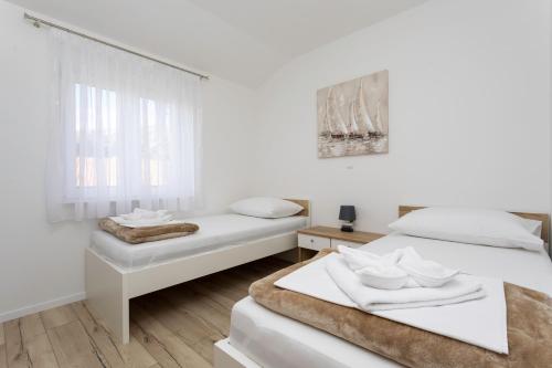 een witte kamer met 2 bedden en een raam bij Apartments Mateo in Baška