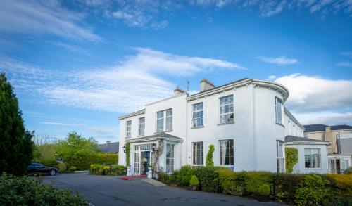 a white house on a street with a blue sky at Castle Oaks House Hotel in Limerick